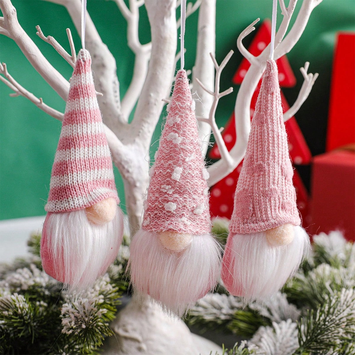 Three knitted gnome ornaments hanging from a branch with a festive background.