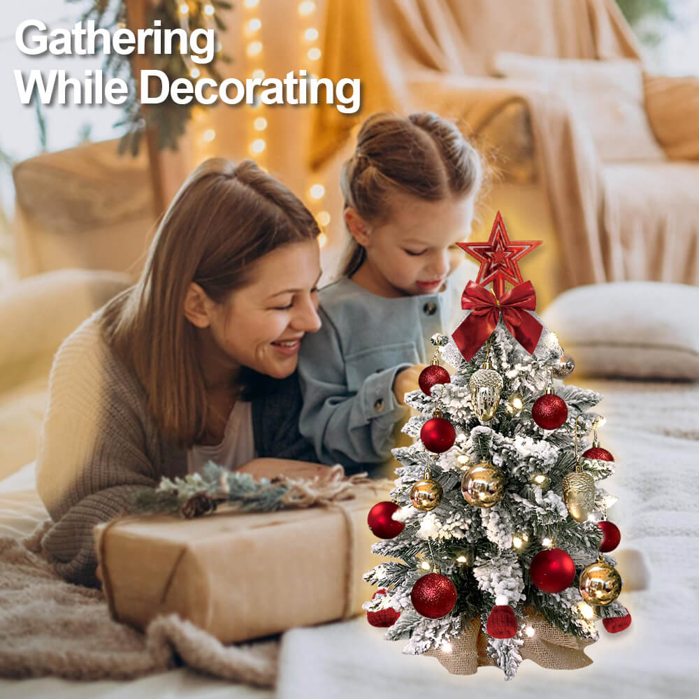 Woman and child decorating a small Christmas tree with red and gold ornaments in a cozy living room.