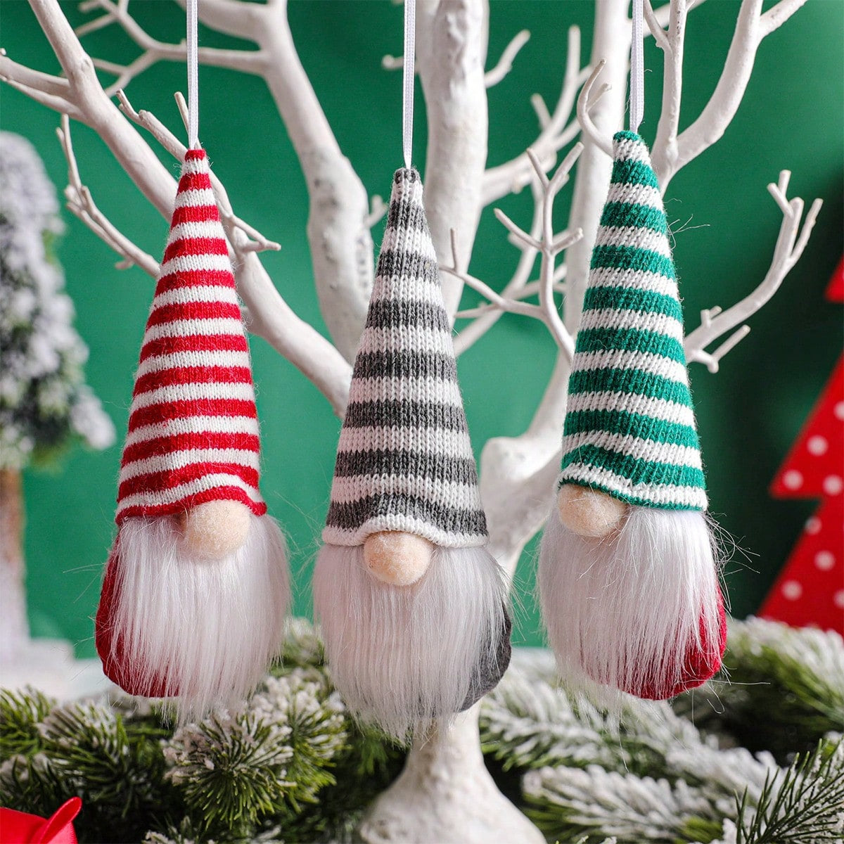 Three striped gnome ornaments hanging from branches with a green background