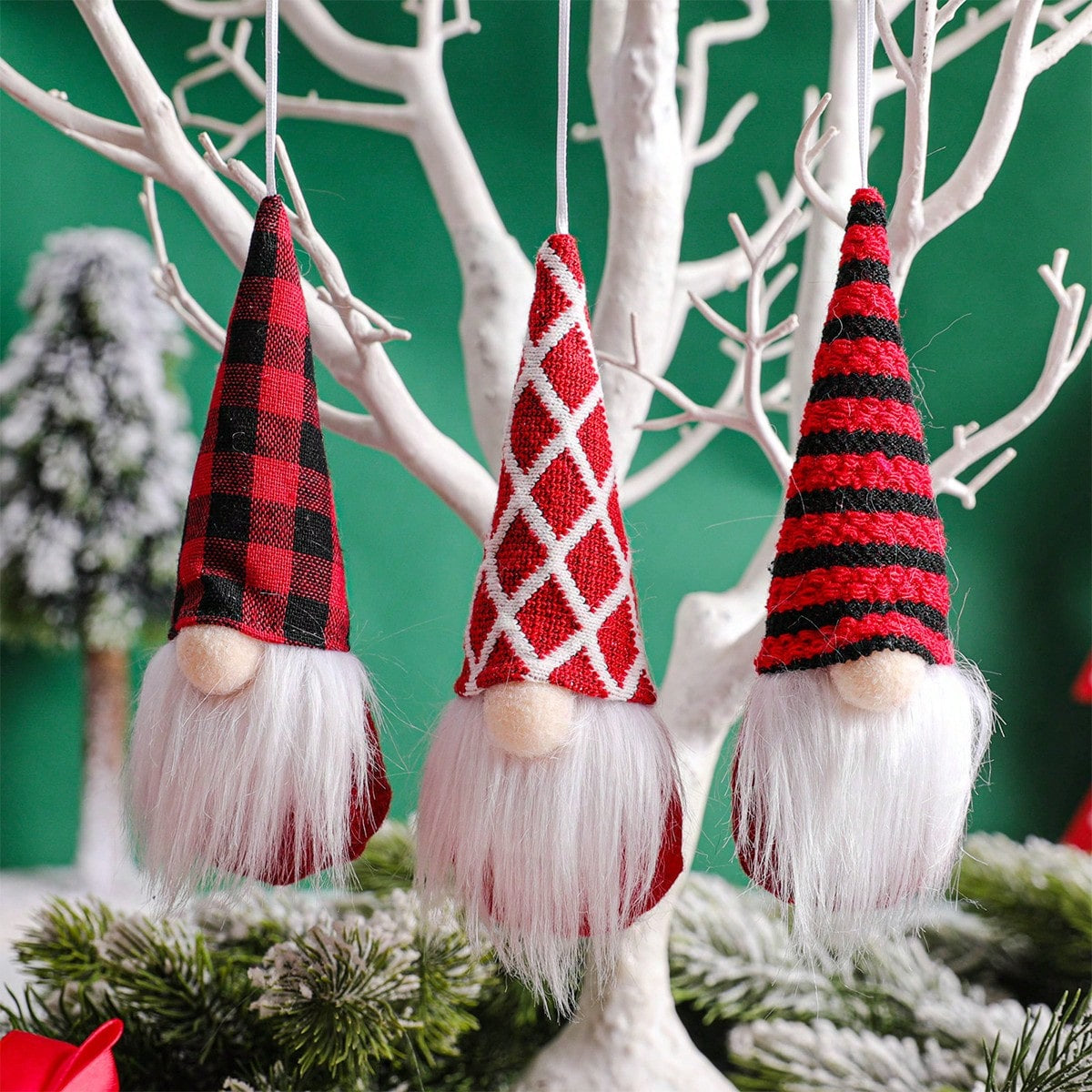 Three gnome ornaments with plaid and patterned hats hanging on a branch.